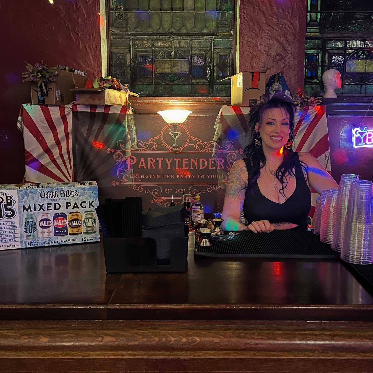 Mandi smiling behind the bar at an indoor venue, Partytender banner behind her