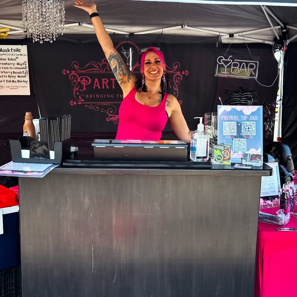 Mandi, pink hair and all, arms up behind the Partytender booth bar