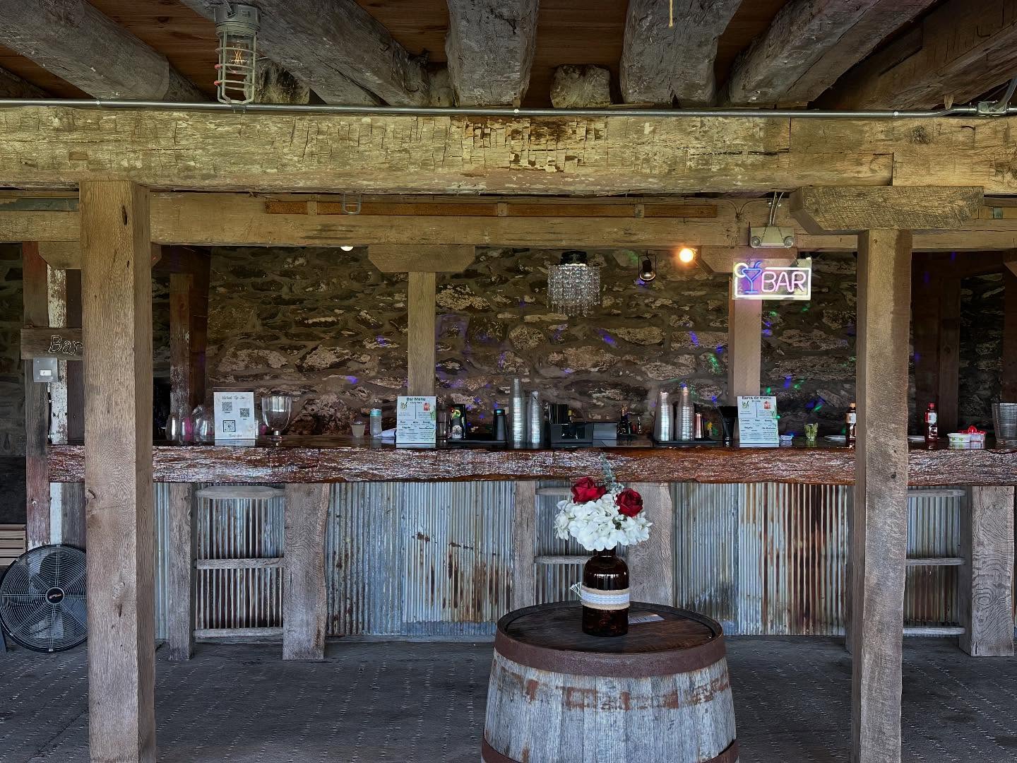 Rustic barn wedding venue bar with chandelier and neon BAR sign, set up by Partytender